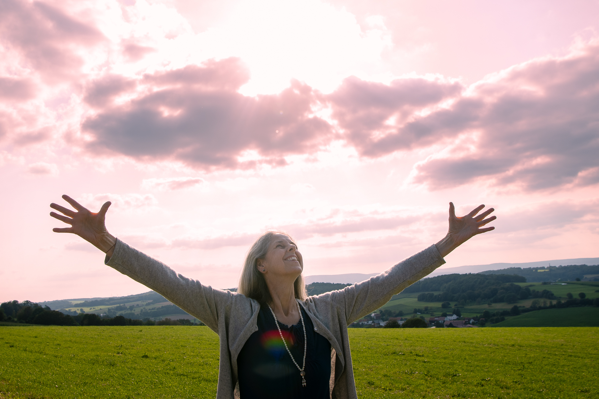 Gunda Ganga steht mit geöffneten Armen in einer Landschaft und hält einen Raum