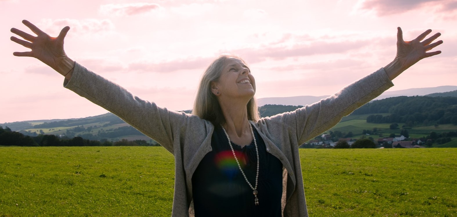 Gunda Ganga steht mit geöffneten Armen in einer Landschaft und hält einen Raum